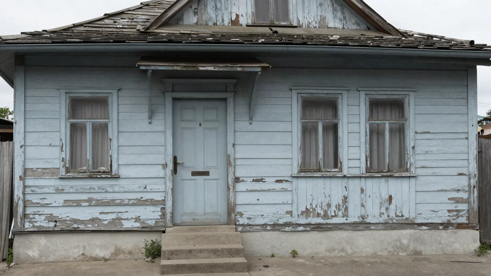 An older house with peeling paint, a sagging gutter and a cracked front step on an overcast day