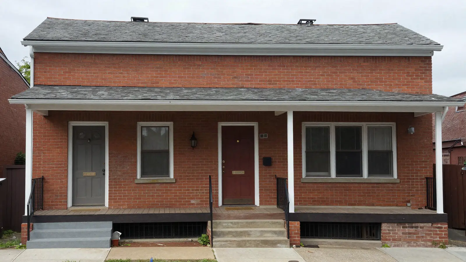 An older brick two-family house with two front doors and a shared front porch on an overcast day