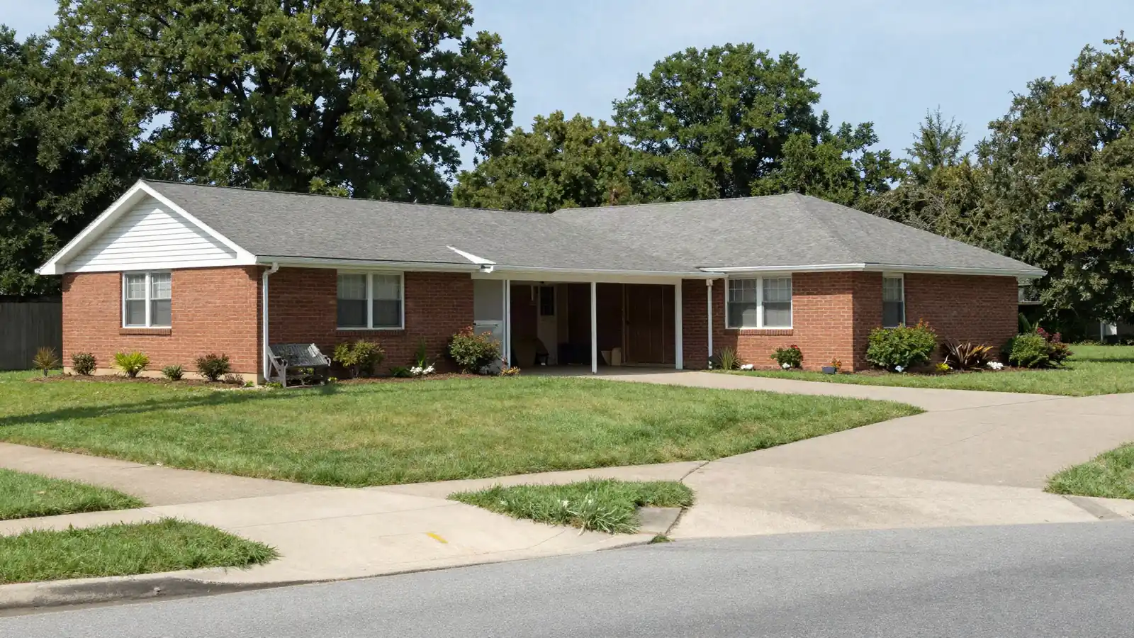 A 1960s brick and siding ranch house with a carport and a wide lawn on a suburban street