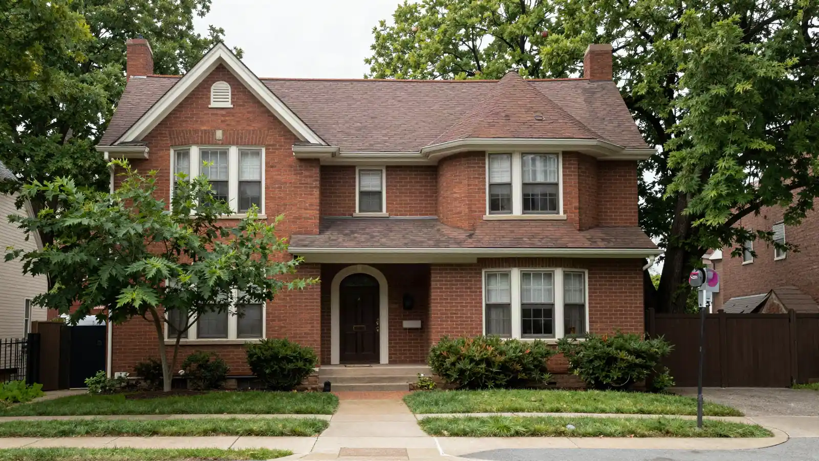 A 1930s brick Tudor-style house with a steep gabled roof and an arched front door on a leafy street