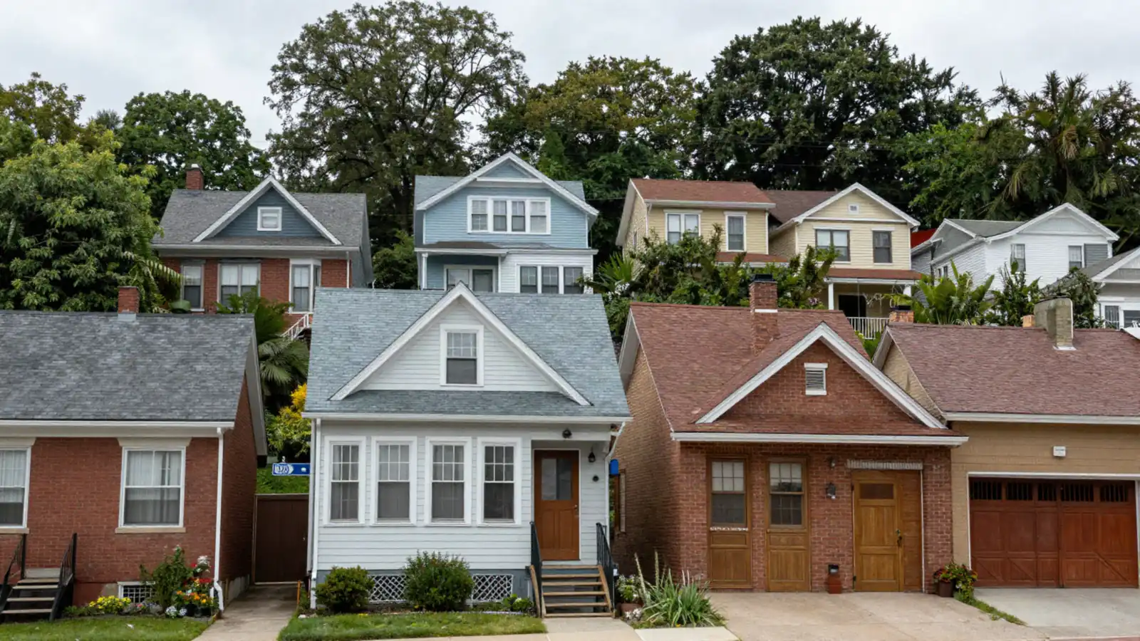 Narrow old frame and brick houses stacked up a steep wooded hillside street on a cloudy day