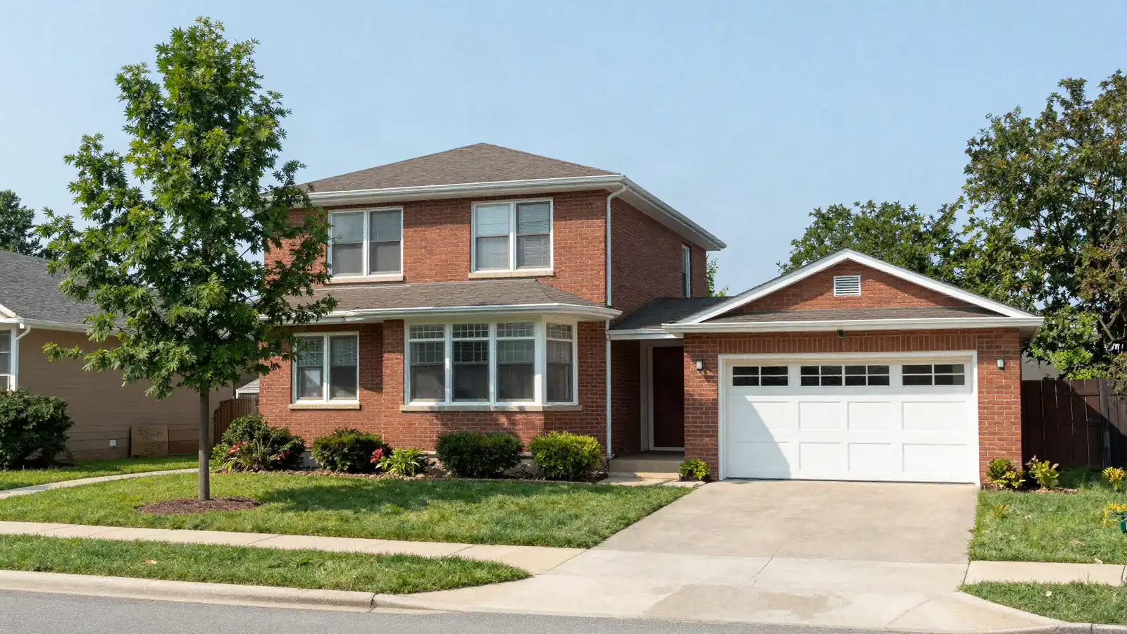 A 1960s brick bi-level house with a large front window and a single garage on a curving suburban street