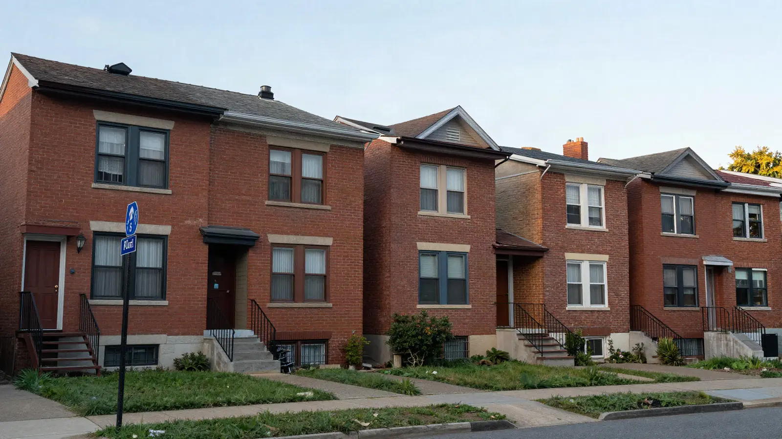 A row of older brick two-family and single-family houses on a city street in late afternoon light